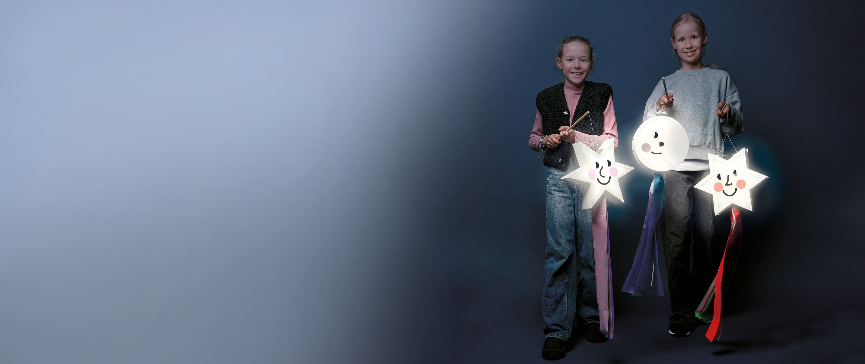 Zwei Kinder halten gebastelte Laternen in Form von Sternen und Mond
