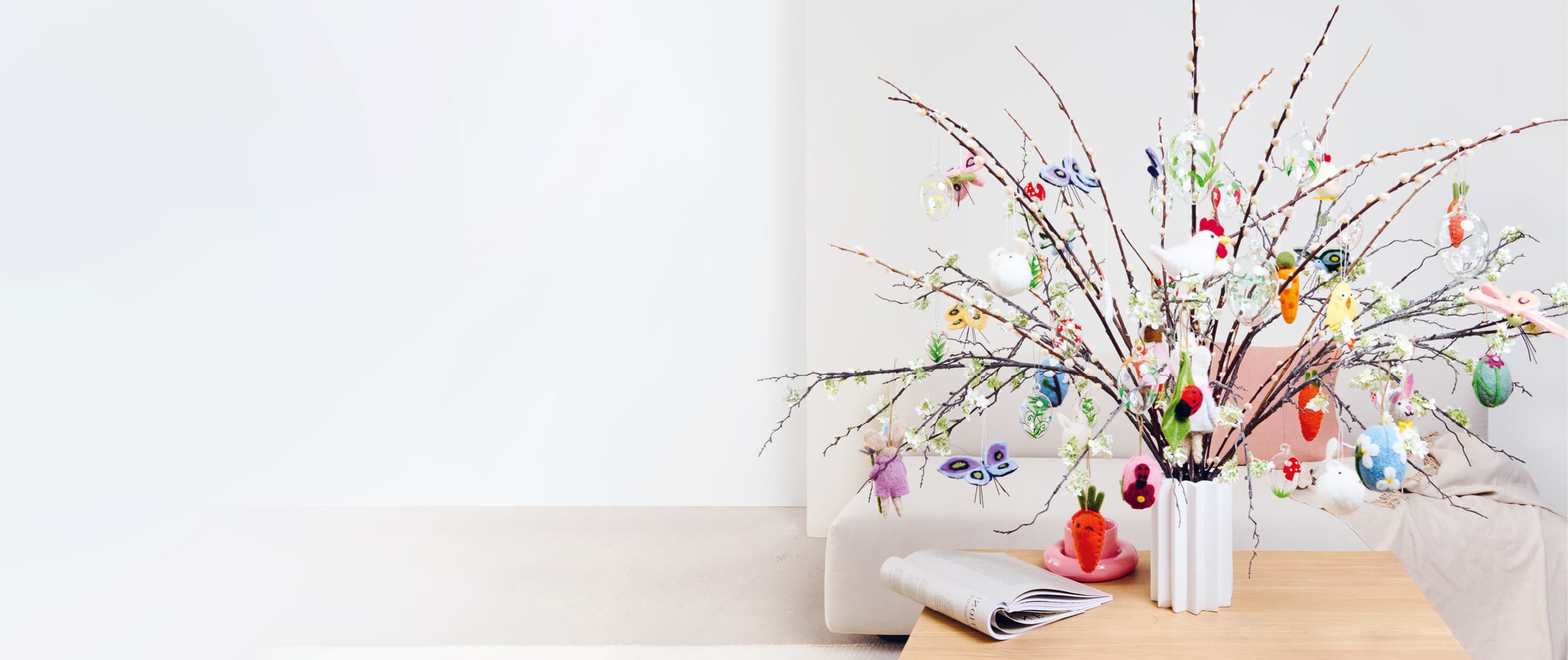 Bunte Anhänger für Ostern und Frühling aus Filz und Glas sind an Zweigen in einer Vase dekoriert. 