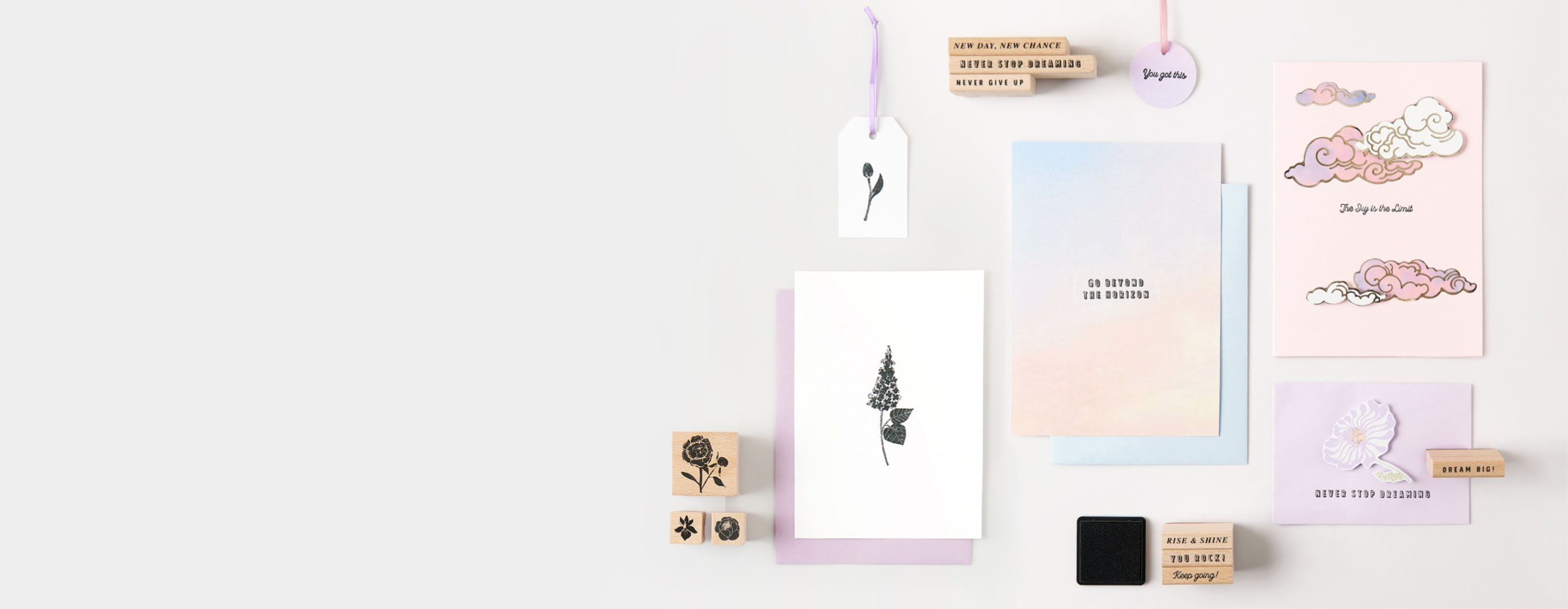 Bestempelte Karten und Geschenkanhänger mit Texten und Blumenmotiven liegen umgeben von Stempeln auf grauem Hintergrund.