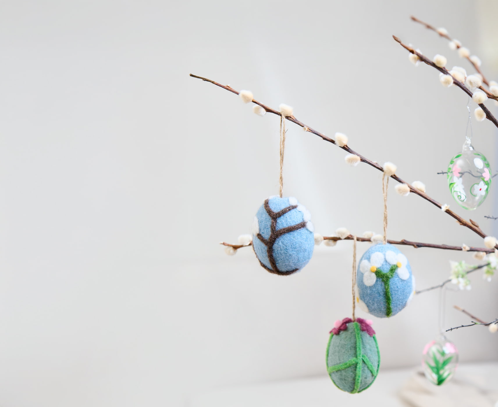 Bunte Ostereier aus Filz hängen an Zweigen in einer Vase.
