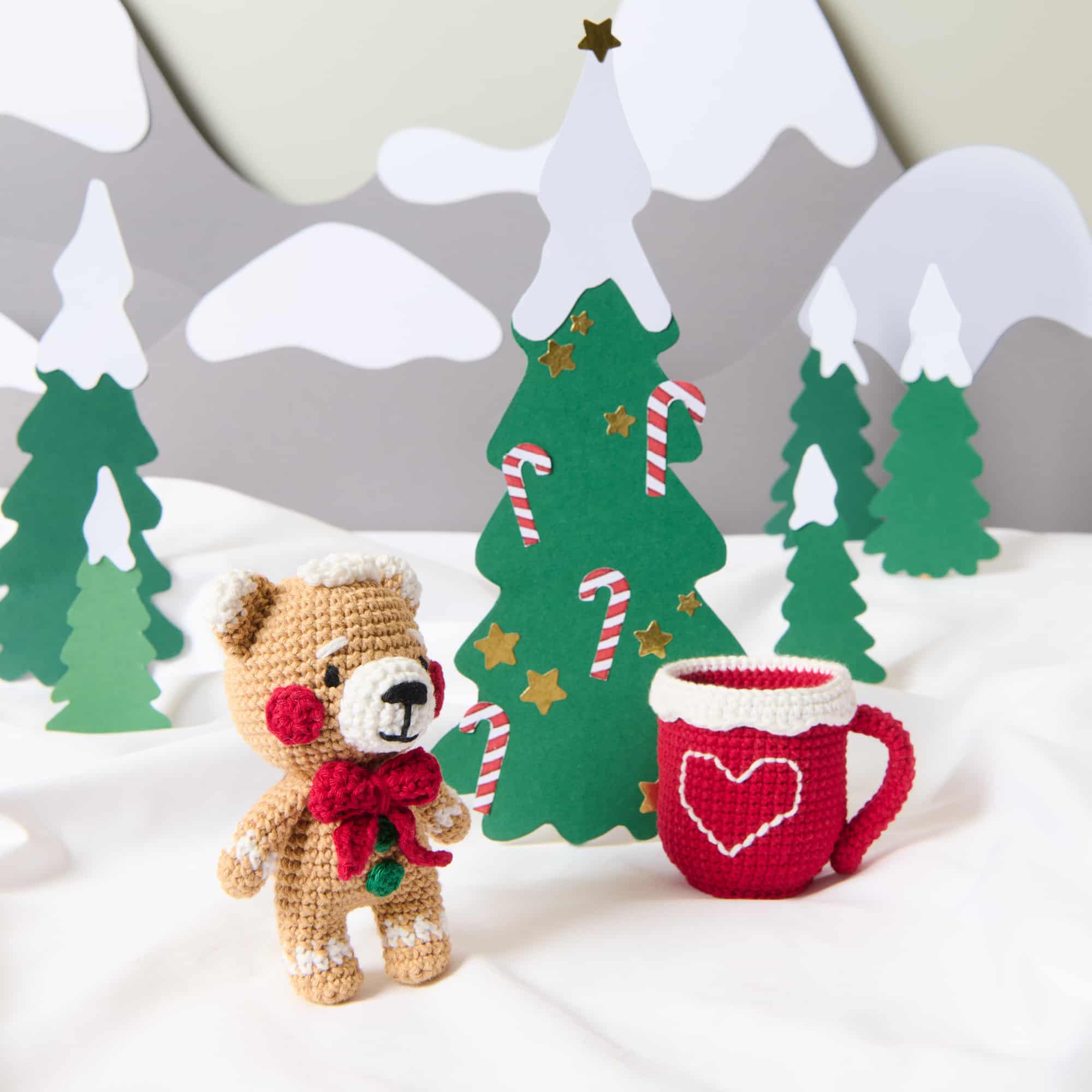 Gehäkelter Bär mit roter Tasse steht in einer Winter-Landschaft.