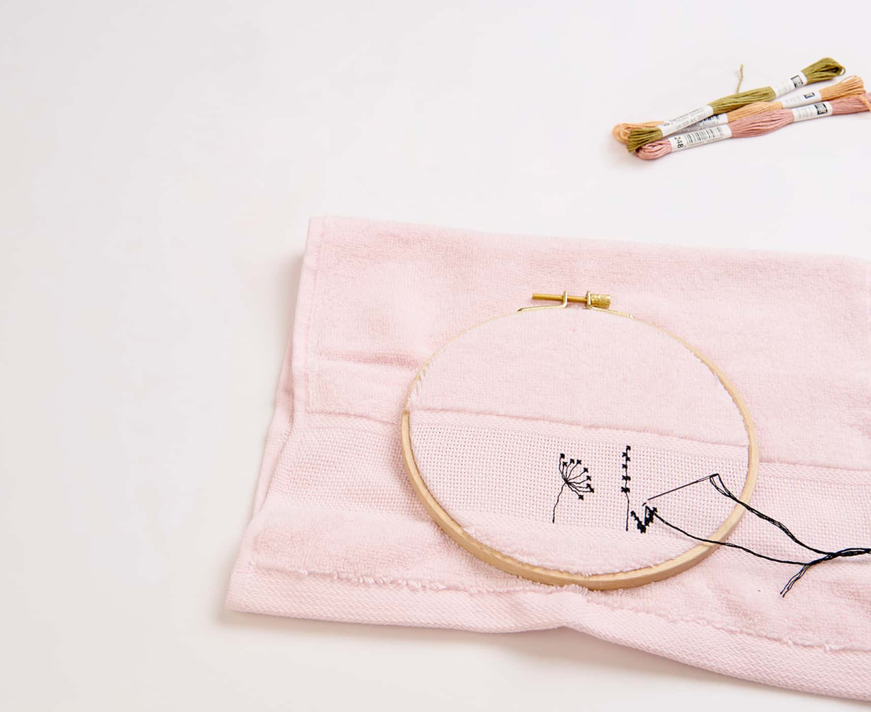 Ein rosa Handtuch wird mit Gräsermotiven bestickt.