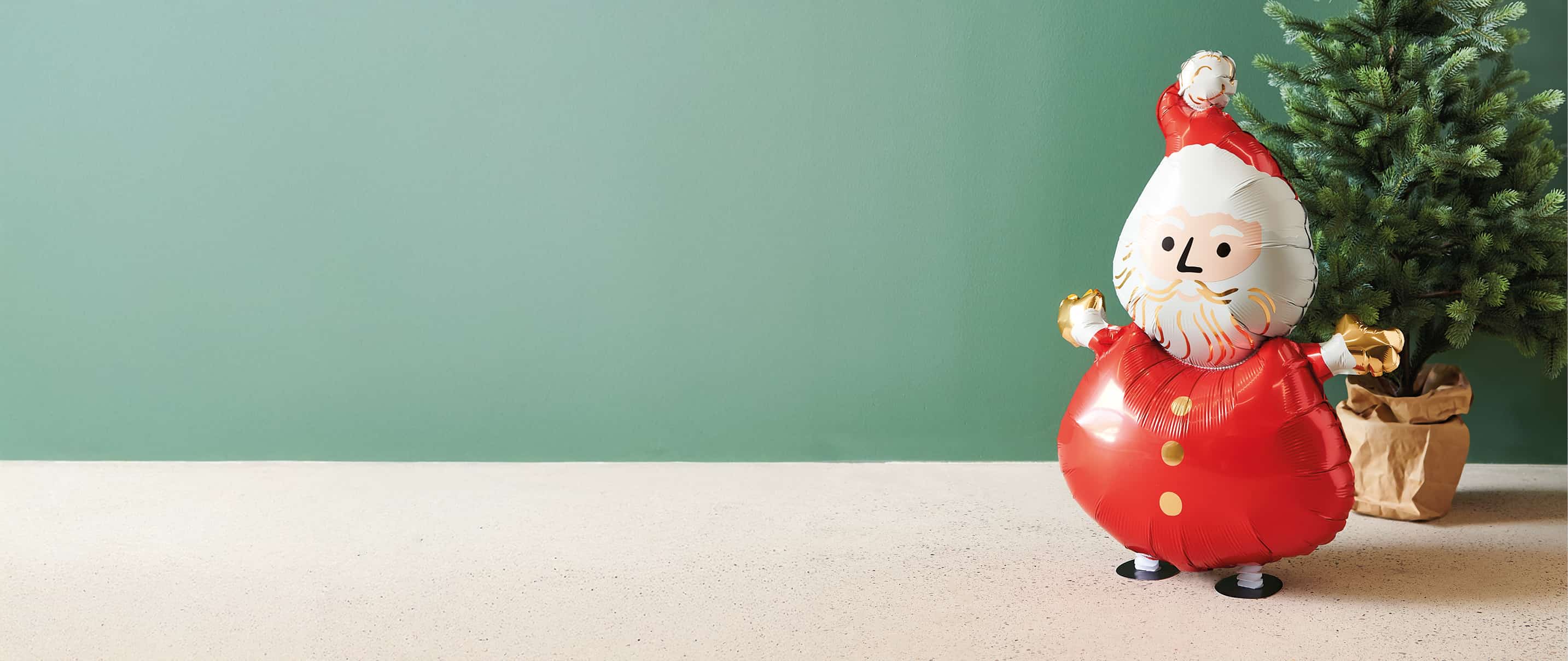 Folienballon in Form eines Weihnachtsmanns vor grünem Hintergrund und Tannenbaum