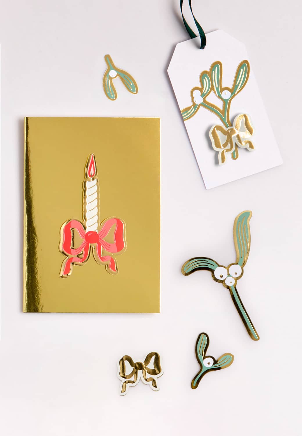 Eine goldene Karte und ein Anhänger sind weihnachtlich mit Glanzbildern in Form von Schleifen und Mistelzweigen dekoriert.